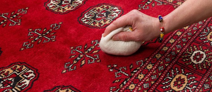 A spot on a red rug being treated by hand before washing