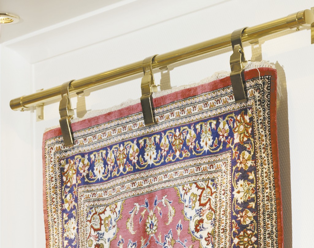 An Oriental rug hung on a wall with a brass rod and clamps